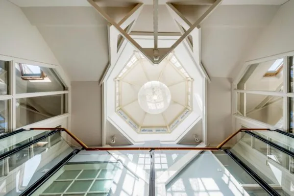 Glazen trapopgang met zicht op een achthoekige lichtkoepel en moderne hanglamp in de Prof. Tulpstraat.